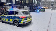 Zwei Polizeifahrzeuge mit Blaulicht stehen in einer beschneiten Straße vor einem Haus 