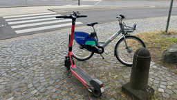 Das Bild zeigt einen am Wegesrand abgestellten E-Scooter und ein Leihfahrrad. 