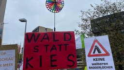 Demonstranten halten Schilder hoch auf denen "Wald statt Kies" und "Keine weiteren Baggerlöcher" steht.