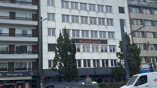 Blick auf die weiße Außenfassade des Hotels, es handelt sich um ein mehrstöckiges Haus in der Großstadt