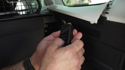 Auf dem Foto sind ein fingerlanger GPS-Tracker und eine geöffnete Seitenwand eines Autokoferraums.
