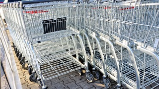 Auf dem Foto sind mehrere Einkaufswagen, die ineinandergeschoben in ihrem Depot vor einem Supermarkt stehen.