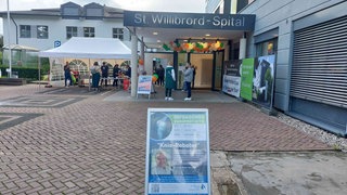 Vor dem Krankenhaus sind Pavillions aufgebaut, der Schriftzug "St. Willibrord-Spital" ist über dem Eingang zu lesen, daran hängen Luftballons