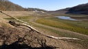 Auf dem Foto ist ein eingerissener Staudamm, dahinter ein Bett eines Sees ohne Wasser.