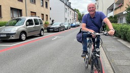 Ein Mann sitzt auf seinem Fahrrad und hält am Bürgersteig der Fahrradstraße 