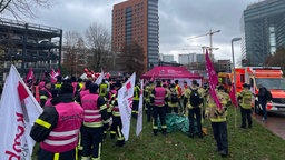 Feuerwehrleute stehen mit Warnwesten, Fahnen und in voller Montur bei ihrer Mahnwache.