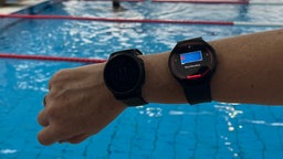 Ein Mitarbeiter träft eine Smartwatch, die eine Karte des Schwimmbads mit einem roten Punkt zeigt.