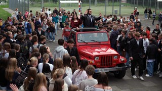 Schüler stehen um die einfahrende rote Karosse 