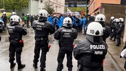 Eine Gruppe von Polizisten schaut auf die Gruppe Demonstrierender, im Hintergrund die Schwebebahn