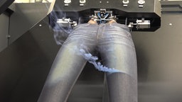 Eine über eine Maschine gespannte Jeans, die durch Laser qualmt