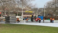 Arbeiter decken die Wiese an der Universität mit grauen Platten ab.