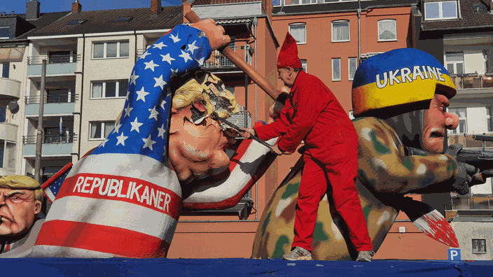 Jacques Tilly, der für den Rosenmontagszug die Mottowagen baut, schwingt ein Brecheisen und trifft den Kopf einer überdimensionalen Pappmaché - Figur von Donald Trump