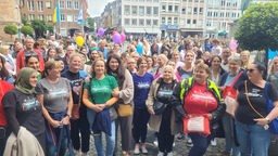 Eine größere Gruppe von Frauen mit bunten T-Shirts und Luftballons, versammelt auf einem Platz