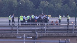 Klimaaktivisten sitzen auf dem Rollfeld, um sie stehen zahlreiche Polizisten.