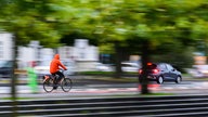 Auf dem Foto ist ein Fahrradfahrer, der auf einer Straße hinter einem Auto fährt.