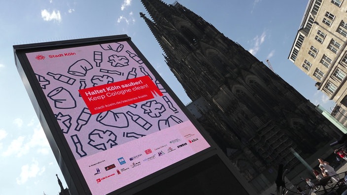 Anzeigetafel mit der Aufschrift "Haltet Köln sauber!", im Hintergrund der Kölner Dom.