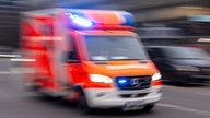 Auf dem Foto ist ein Krankenwagen der Feuerwehr mit Blaulicht, der über eine Straße fährt.