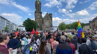 Zahlreiche Menschen haben sich vor einer Kirche versammelt und halten Flaggen hoch.