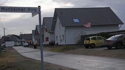 Straßenschild "Manheimer Ring" auf der linken Seite, rechts Weg mit Häuserreihe 