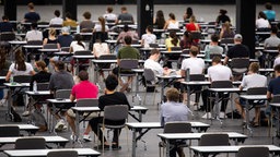  Studenten und Studentinnen sitzen an Tischen in einer Messehalle der KölnMesse und warten auf den Beginn ihrer Klausur.