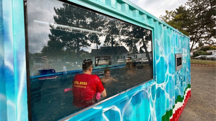 Ein Helfer der DLRG bringt Kindern in einem Schwimmcontainer das Schwimmen bei.