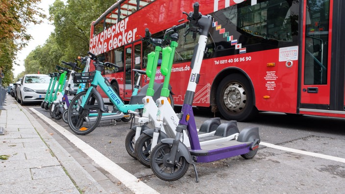 Eine in weiß eingerahmte Fläche auf der Straße. In der Fläche stehen E-Scooter und Fahrräder.