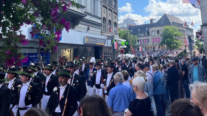 Viele Schützen laufen beim Umzug durch die Stadt, Zuschauer am Rand schauen zu 