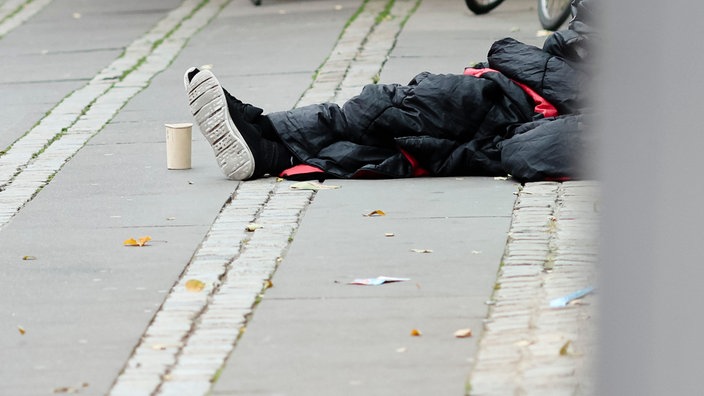 Symbolbild: Ein Mann sitzt in einen Schlafsack gehüllt auf dem Asphalt.