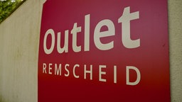 Rotes Schild mit Schriftzug "Outlet Remscheid" an weißer Wand