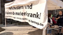 Weißes Banner mit "Verkehrslärm und Feinstaub machen krank! - Bürgerinitiative Lennep". Dahinter Mann mit Mikrophon in der Hand