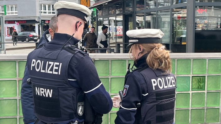 Zwei Polizeibeamte kontrollieren in der Öffentlichkeit einen Mann