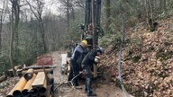 Zwei Arbeiter führen Bohrungen in einem Wald durch.