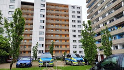 Auf dem Foto ist ein zehnstöckiges Hochhaus, davor stehen zwei Polizeiwagen.