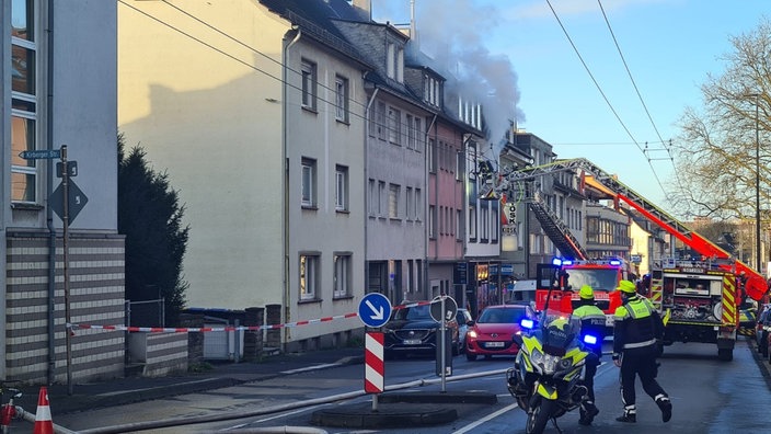 Aus einem Haus kommt Rauch. Auf der STarße steht ein Polizeimotorrad und ein FEuerwehrauto.