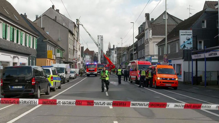 Einsatzfahrzeuge stehen vor einem Haus, im Hintergrund eine Drehleiter vor einem Haus.