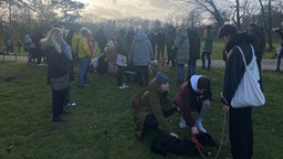 Das Foto zeigt die Menschen und Hunde die sich beim Bark-Date auf einer Wiese getroffen haben. 