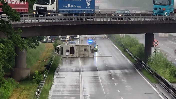 Ein Wohnmobil ist umgekippt und liegt auf der Fahrbahn, dahinter stehen Polizeiautos mit Blaulicht