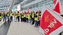 Menschen mit Warnweste und Verdi-Flagen in großer Halle des Düsseldorfer Flughafens