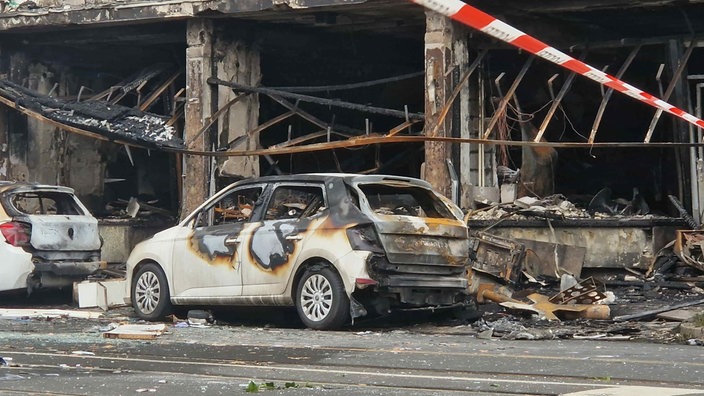 Nähere Aufnahme eines fast vollständig ausgebrannten Autos vor dem ausgebrannten Haus.