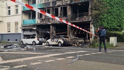 Ein zum Teil angebranntes und ein fast komplett ausgrebranntes Auto vor dem Zerstörten Haus.