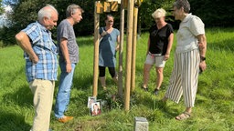 Angehörige stehen um einen Baum, an dem kleine Bilder und Erinnerungen an die durch Suizid Verstorbenen aufgestellt sind.