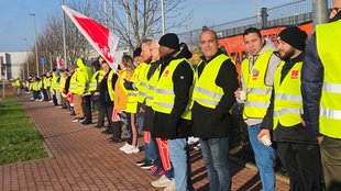 Auf dem Bild sind zahlreiche Menschen vor einem Gebäude nebeneinander zu erkennen. Sie bilden eine Kette.