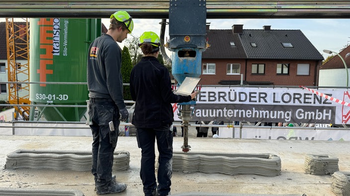 Zwei Bauingenieure stehen an der Düse eines großen 3D-Druckers