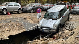 Ein Auto neigt mit der Vorderseite Richtung des Straßenrisses, der sich aufgrund des Wasserrohrbruchs geöffnet hat.