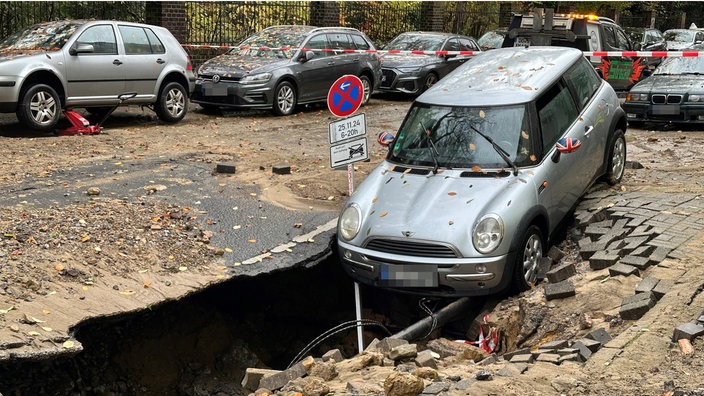 Ein Auto neigt mit der Vorderseite Richtung des Straßenrisses, der sich aufgrund des Wasserrohrbruchs geöffnet hat.