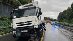 Ein LKW steht auf der Leitplanke. Hinter dem LKW befinden sich Rettungsfahrzeuge. Man sieht eine Vorderansicht.