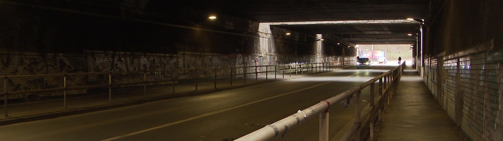 Fußgängerweg durch einen dunklen Tunnel, in der Mitte fahren Autos