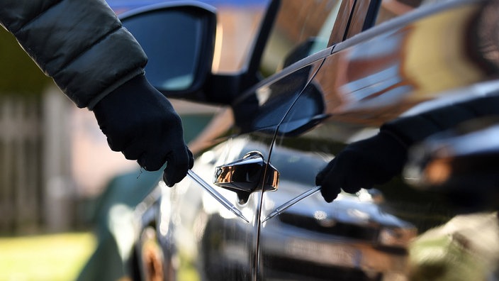 Eine Hand mit einem Schraubenzieher, die den Lack eines Autos zerkratzt