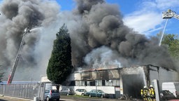 Feuerwehrkräfte kämpfen gegen große, dunkle Rauchwolken an.