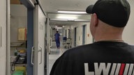 Auf dem Foto ist ein Security-Mann mit einer Kappe, der einen Gang eines Krankenhauses hinunterschaut.